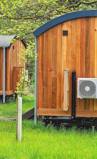 Pods glamping en bois : Confort moderne et nature. Deux pods de glamping en bois, dont un équipé d'une unité de climatisation murale, sur fond de forêt luxuriante et d'herbe verte.